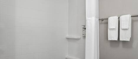Un baño con paredes de azulejos blancos, una cortina de ducha y dos toallas colgadas en un perchero.