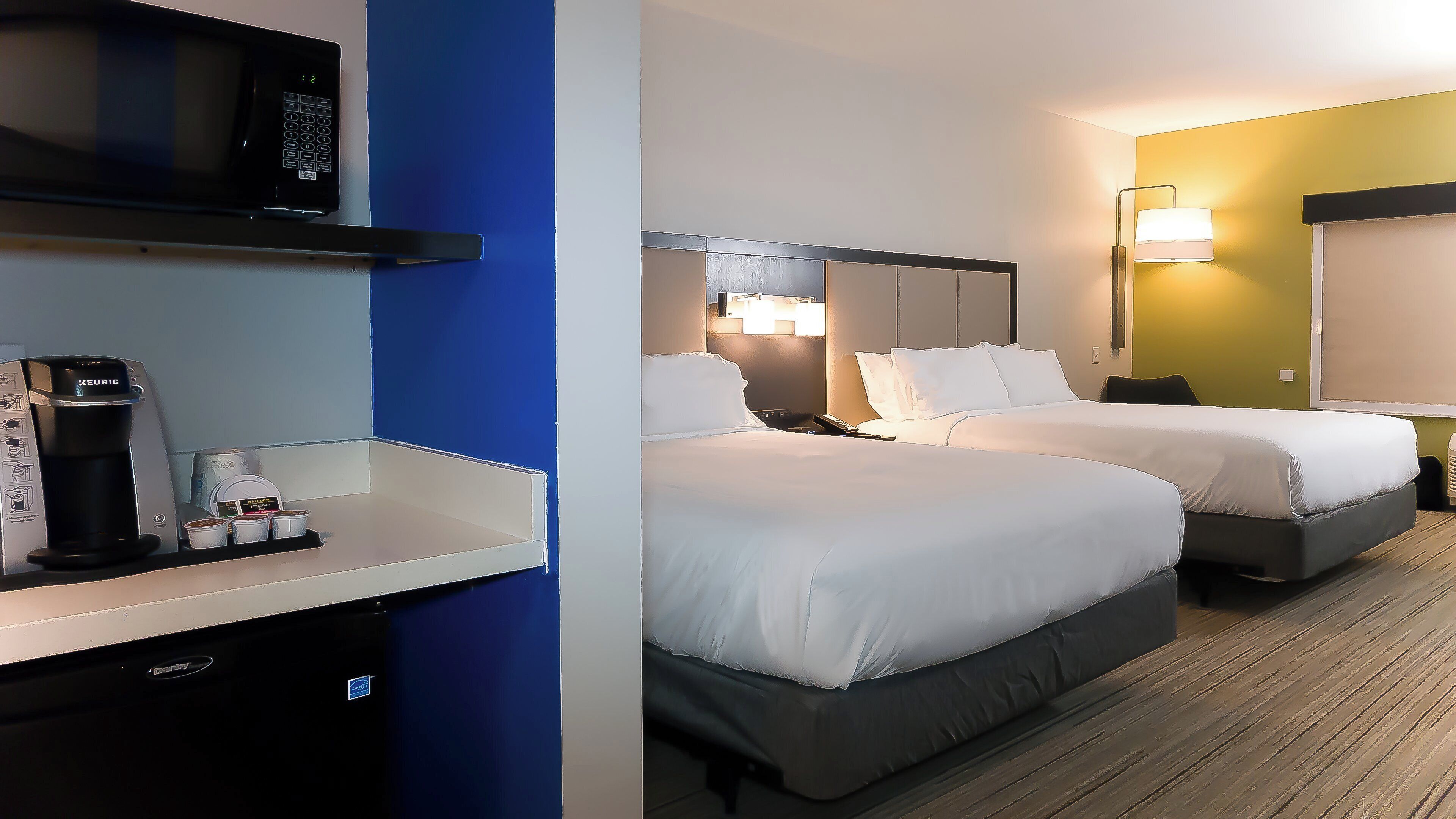 A hotel room with two beds, a minibar, a coffee maker, and a television.