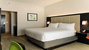 A hotel room with a large bed, a bedside table with a lamp, a wall-mounted artwork, and a door leading to a bathroom.