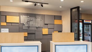 Zona de recepción de un hotel con diseño moderno, incluyendo un letrero de Holiday Inn Express, un mostrador de recepción y un refrigerador lleno de bebidas.