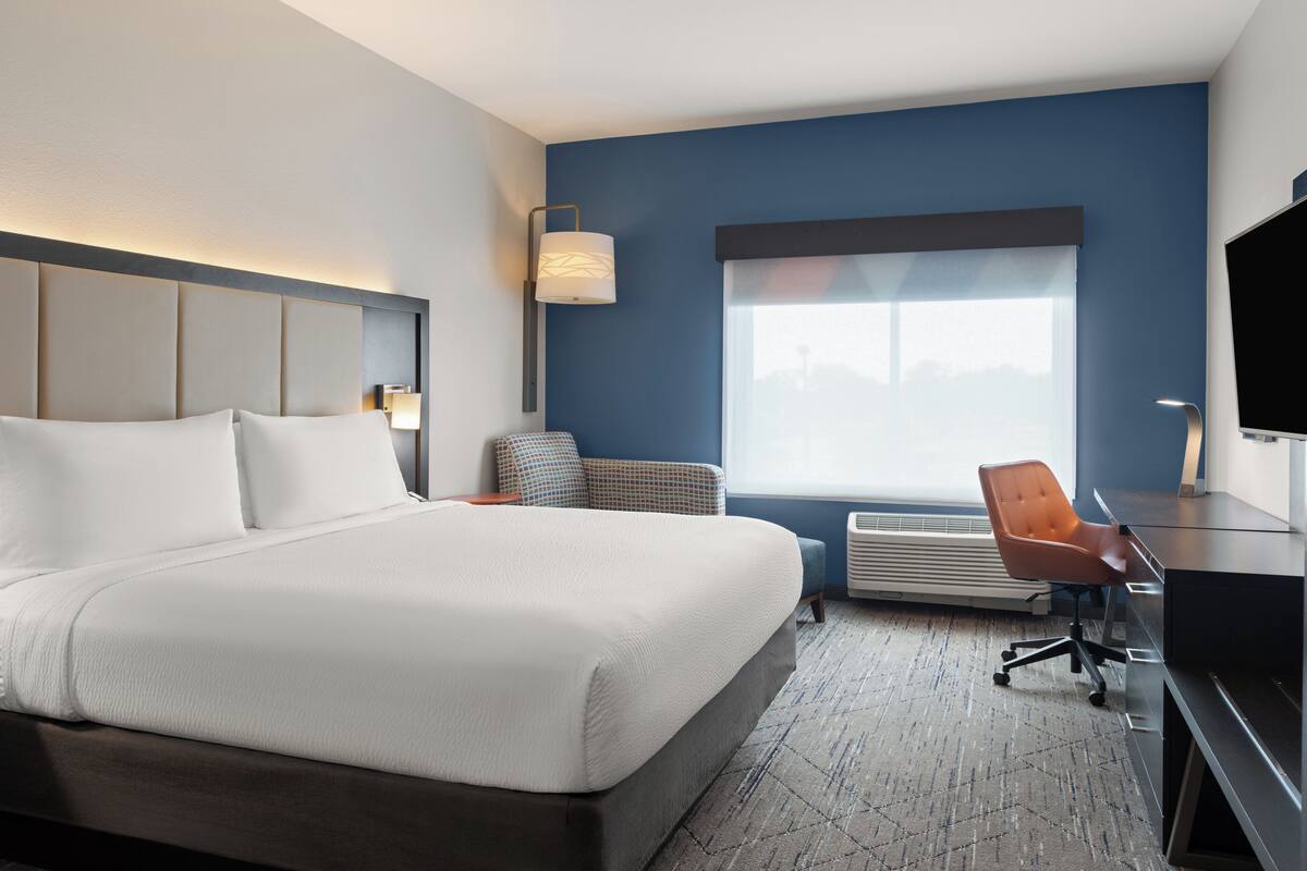 A modern hotel room with a large bed, a desk, a chair, and a television.