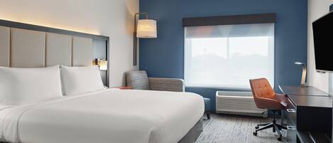 A modern hotel room with a large bed, a desk, a chair, and a television.