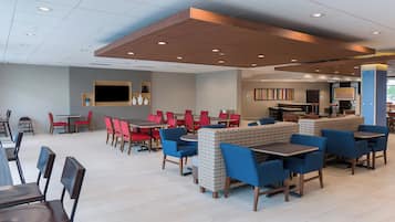 A modern restaurant with high tables and booths, a flat-screen TV, and a variety of seating options.