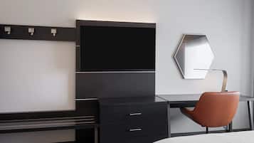 A modern hotel room with a black desk, a brown chair, a flat-screen TV, and a large mirror.