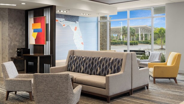 Un moderno vestíbulo de hotel con un sofá, sillones, una mesa de centro y un amplio ventanal con vistas al exterior.