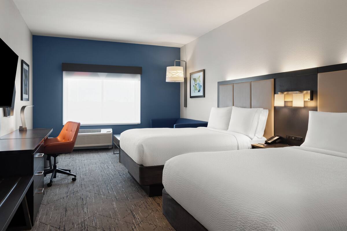 A hotel room with two beds, a desk, a chair, and a large window.