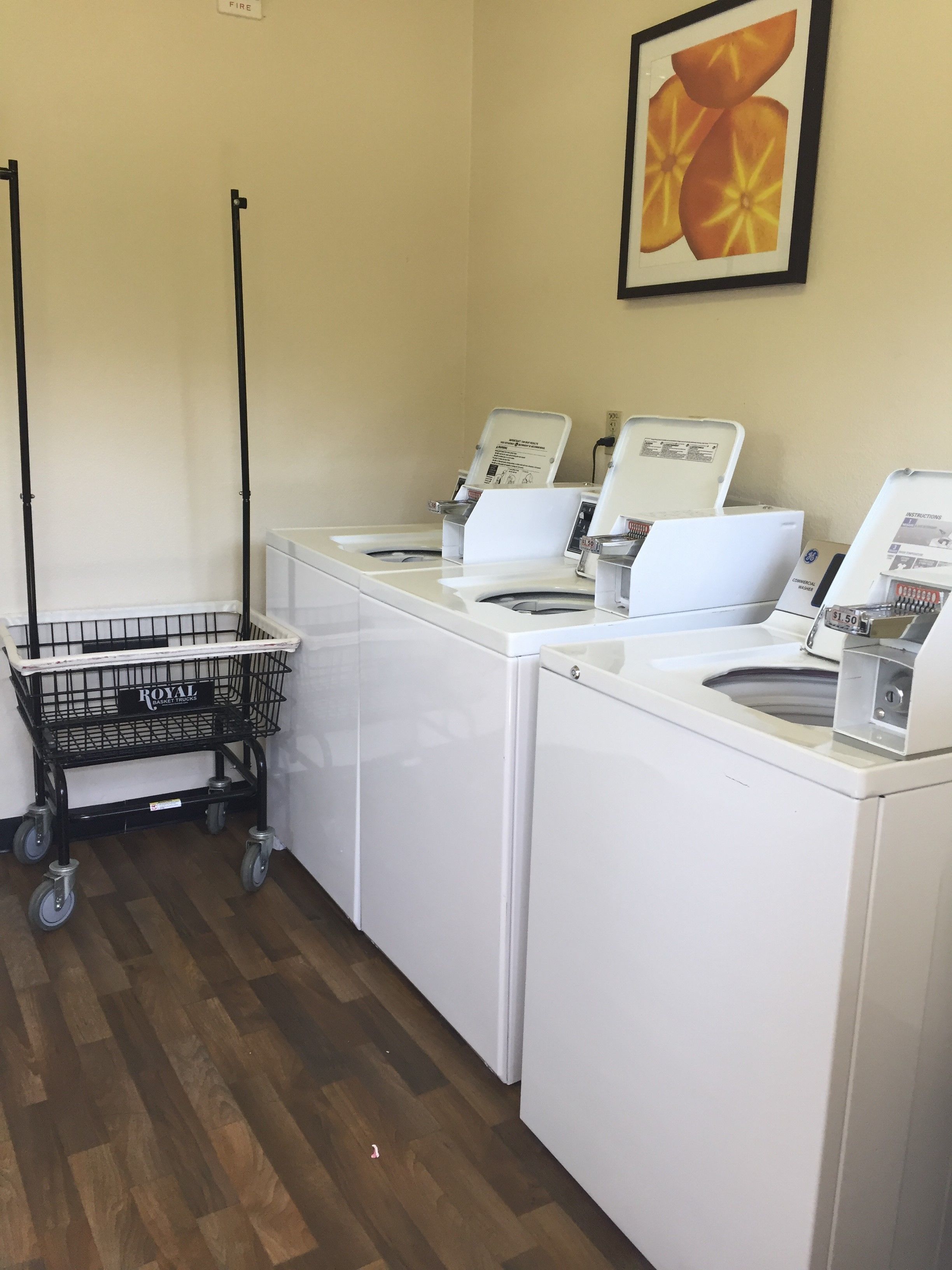 A laundry area with three white washing machines, a black metal cart, and a framed picture on the wall.