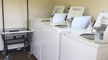A laundry area with three white washing machines, a black metal cart, and a framed picture on the wall.