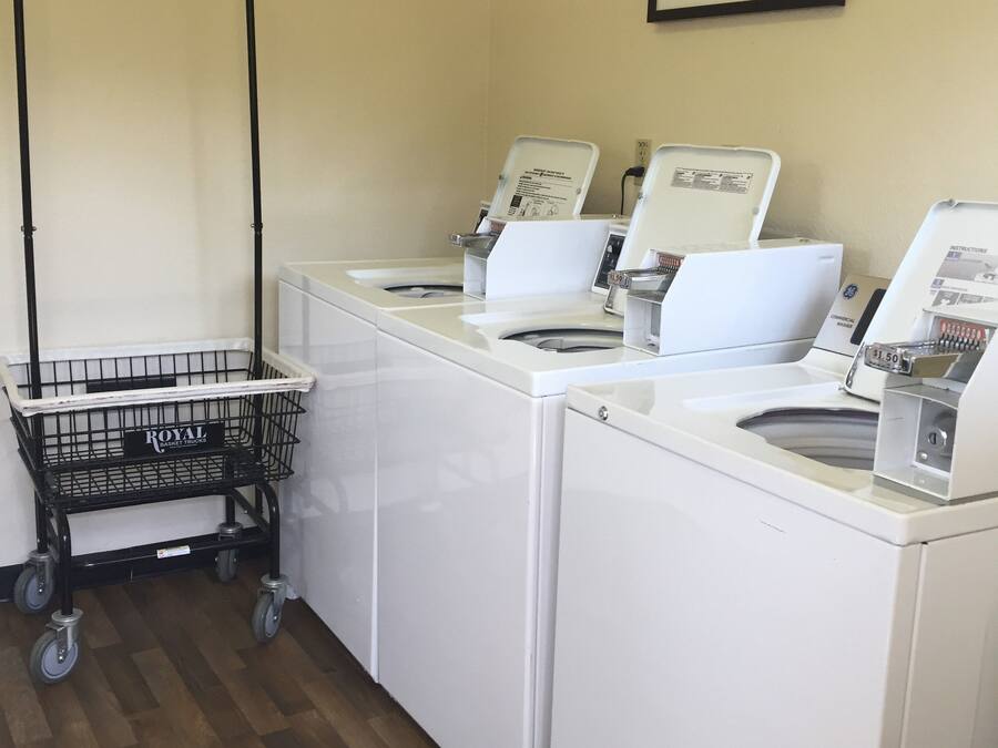 A laundry area with three white washing machines, a black metal cart, and a framed picture on the wall.