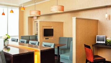 A hotel lobby with a reception desk, seating area, television, and a small table with a monitor.
