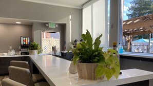 Un espace d’accueil moderne avec un grand comptoir blanc, plusieurs chaises, une plante en pot, un distributeur automatique et une vue sur l’extérieur grâce à de grandes fenêtres.