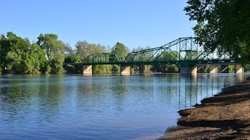 Eine grüne Metallbrücke über einem ruhigen Fluss, gesäumt von Bäumen auf beiden Seiten.