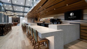 A modern bar area with a long counter, multiple bar stools, and a television screen displaying the DoubleTree logo.