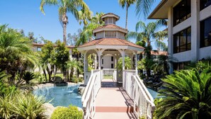 A gazebo with a tiled roof, surrounded by palm trees and a swimming pool.