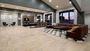 A spacious lobby with a modern design, featuring a seating area with sofas and chairs, a dining table, and a large TV screen.