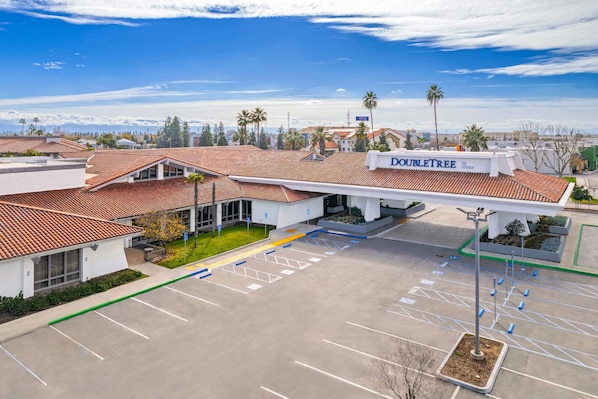 A hotel with a red-tiled roof, a sign reading "DOULETREE," and a parking lot with marked spaces.