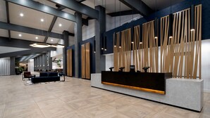 A modern hotel lobby with a reception desk, seating area, and high ceilings.