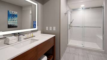 A modern bathroom with a large mirror, white sink, and a glass-enclosed shower.