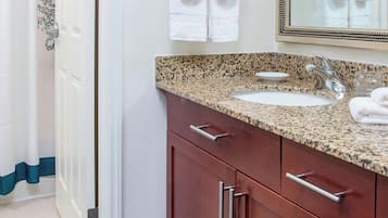 A bathroom with a granite countertop sink, a mirror, and wooden cabinets.