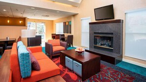 A hotel lobby with a sofa, chairs, a coffee table, a fireplace, and a television. - Residence Inn by Marriott Topeka (Topeka)