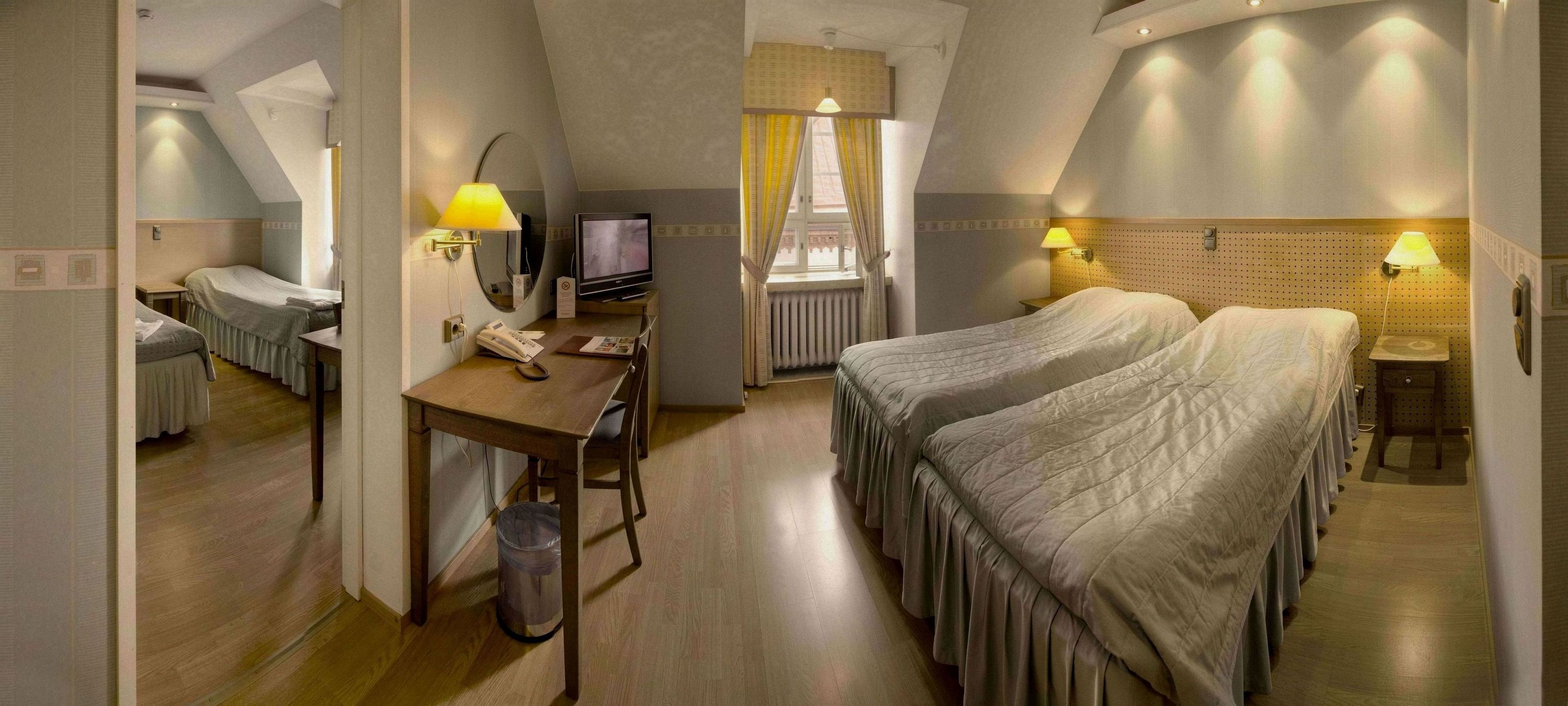 Une chambre d’hôtel avec deux lits, un bureau avec un ordinateur, un téléphone et une poubelle.