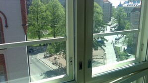 Vista a través de una ventana de múltiples paneles que muestra una calle con árboles, edificios y una carretera.