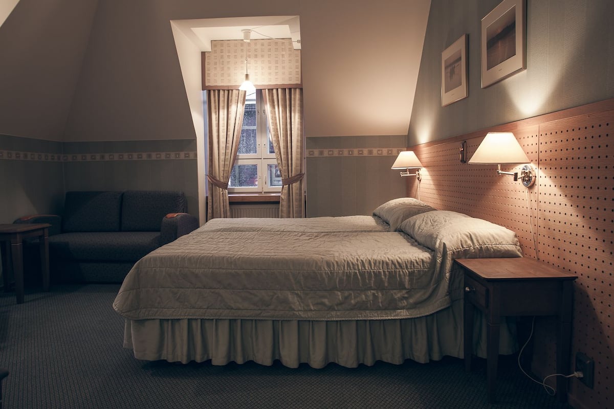 A hotel room with a large bed, a sofa, a desk, and a window with curtains.