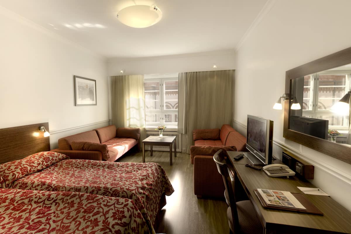 A hotel room with two beds, a desk with a TV, a chair, a small table with a vase, and a window with curtains.