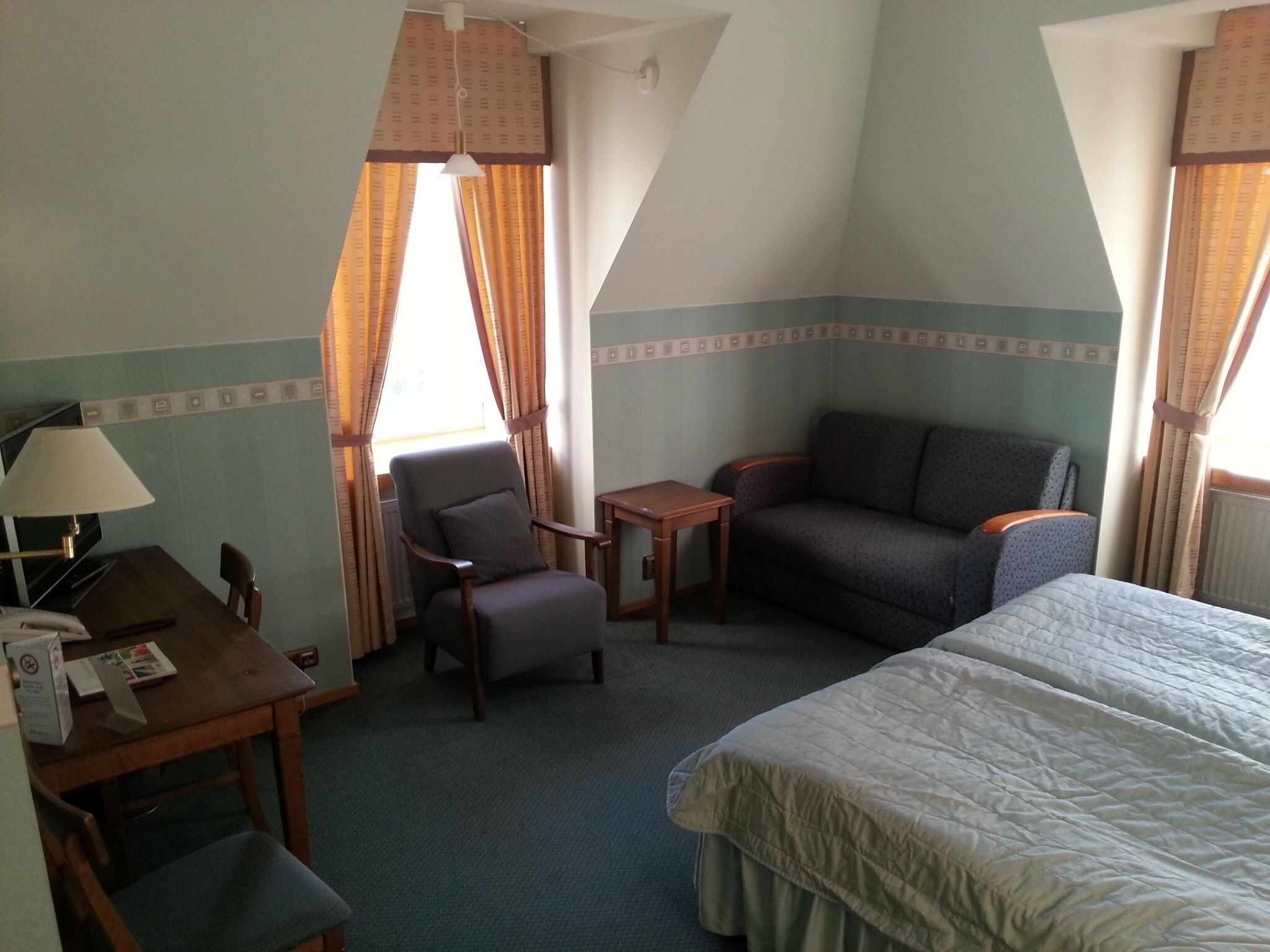 A hotel room with a bed, a desk with a lamp, a chair, a small table, and a sofa.