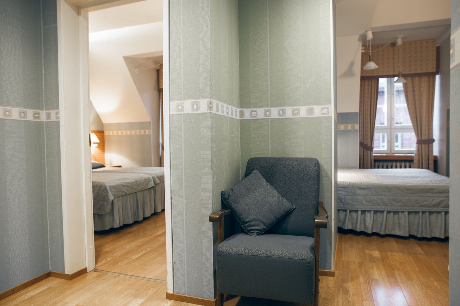 A hotel room with two beds, a chair, and a window with curtains.