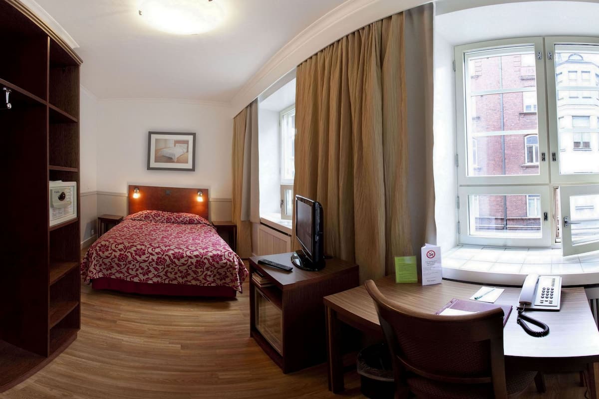 A hotel room with a bed, a desk, a TV, and a window with curtains.
