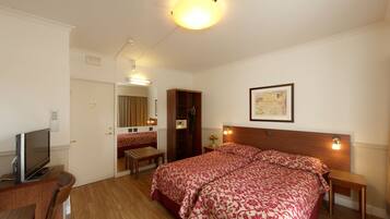Una habitación de hotel con cama, mesitas de noche, televisión, escritorio y espejo.