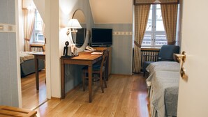 Una habitación de hotel con escritorio de madera, cama, televisor y ventana con cortinas.