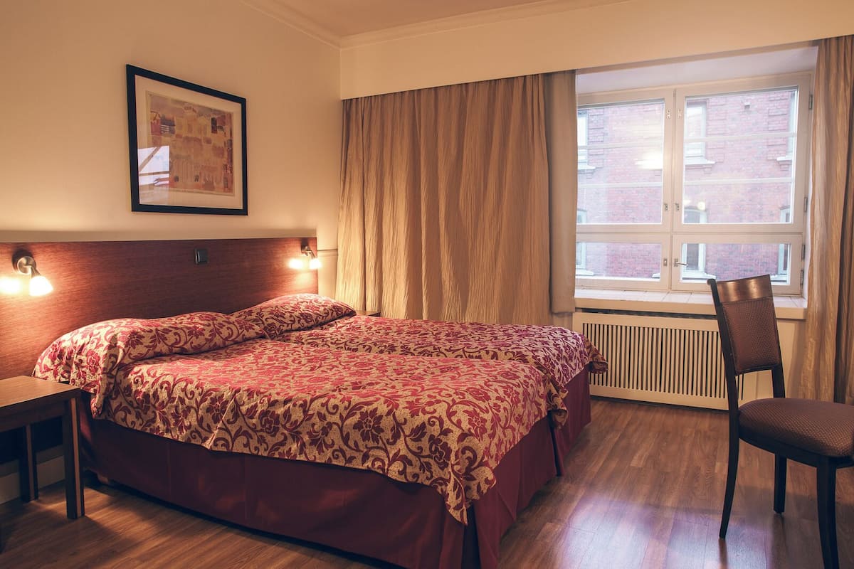 A hotel room with a large bed, a chair, a desk, and a window with curtains.