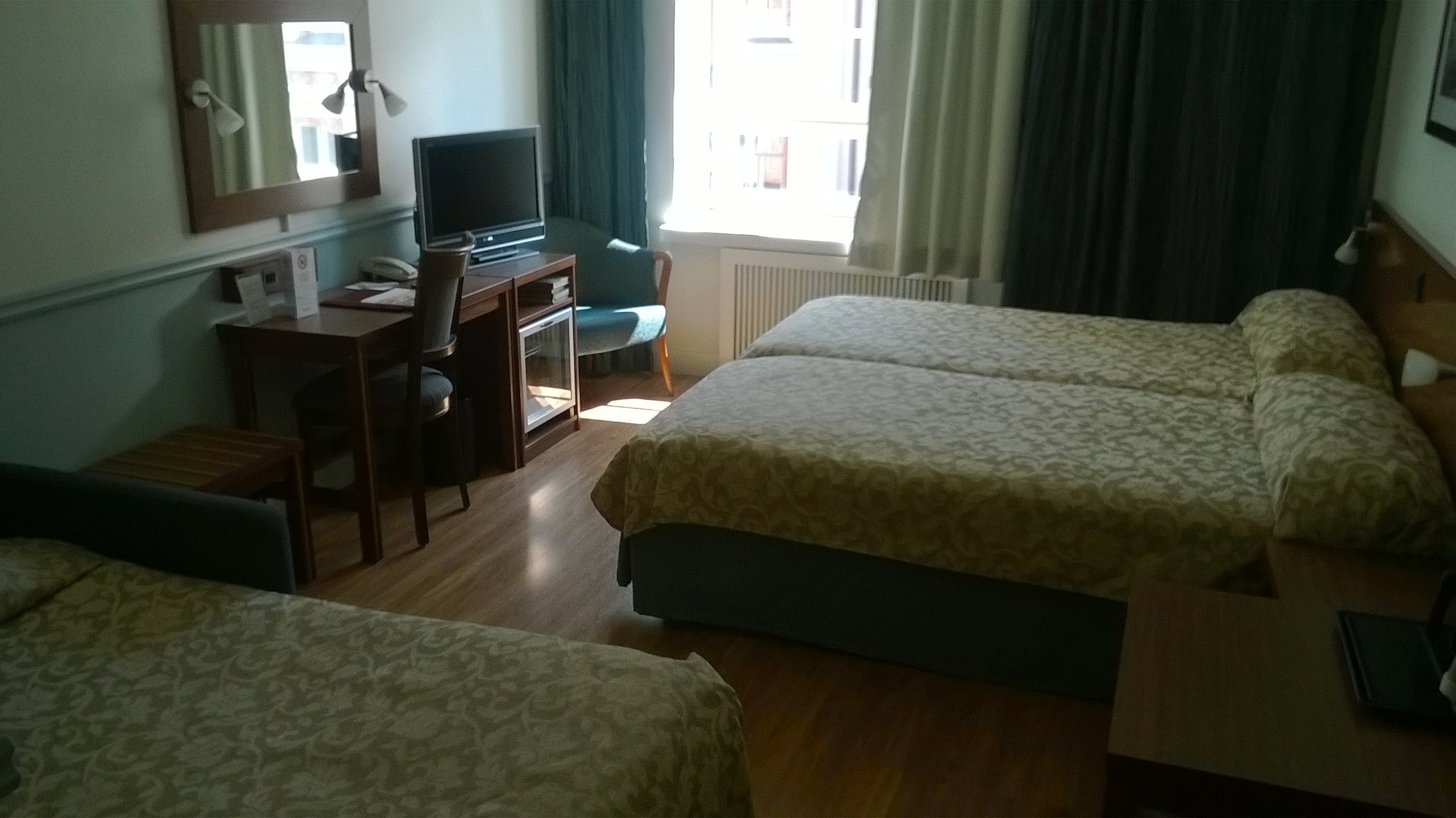 Habitación de hotel con dos camas, un escritorio con computadora, una silla y un ventanal con cortinas.