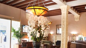 A lobby with a large vase of white flowers, a wooden ceiling, and a tiled floor. - Hotel Carmel (Santa Monica)