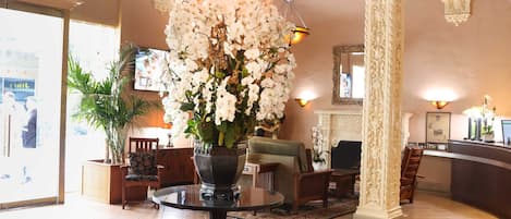 A lobby with a large vase of white flowers, a wooden ceiling, and a tiled floor.