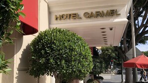A hotel entrance with a red awning, a sign reading "HOTEL GARMEL", and potted plants along the walkway. - Hotel Carmel (Santa Monica)