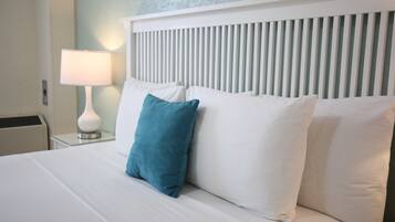 A neatly made bed with white and teal pillows, a white headboard, and a bedside lamp.