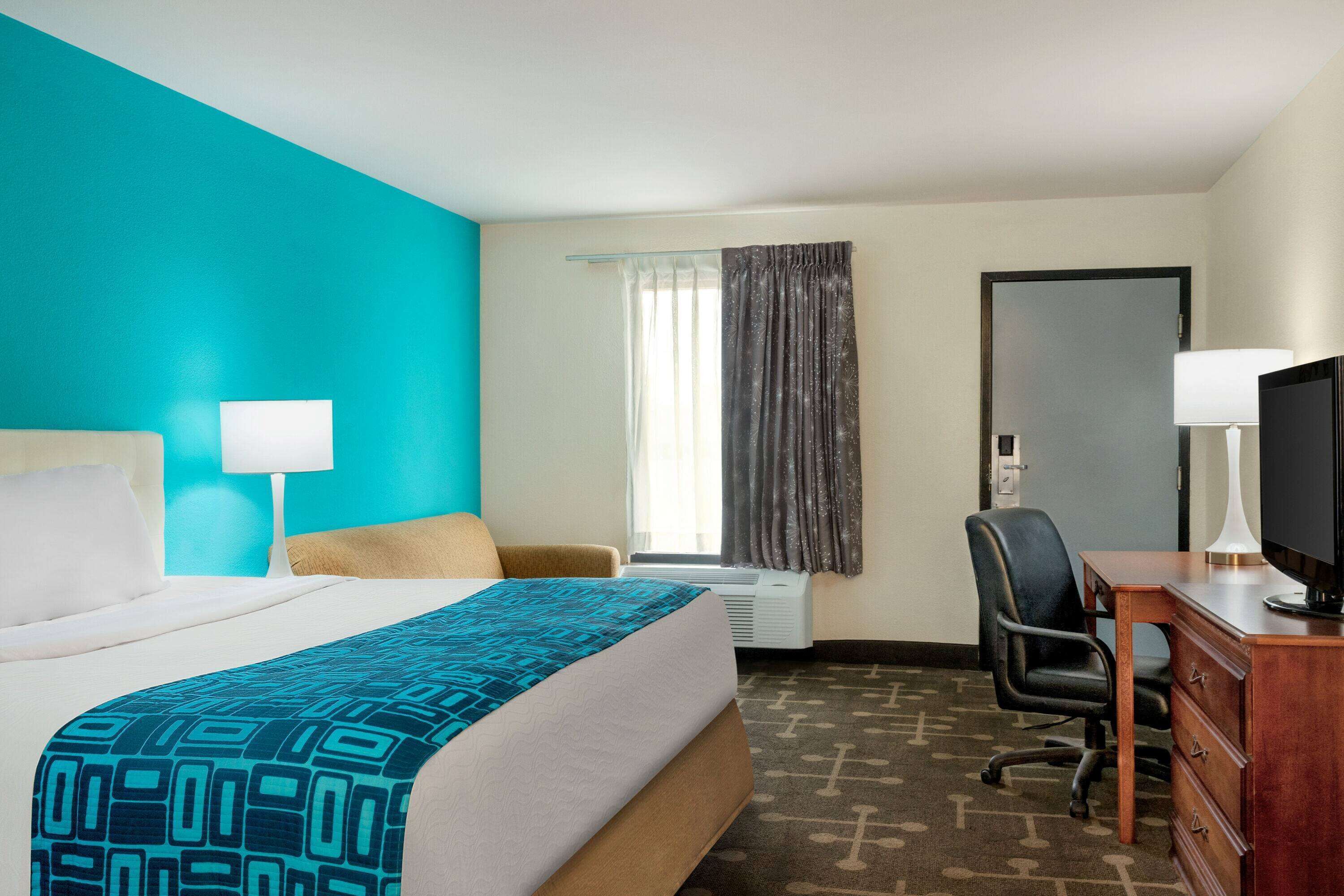 A hotel room with a bed, a desk, a chair, a television, and a window with curtains.