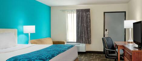 A hotel room with a bed, a desk, a chair, a television, and a window with curtains.