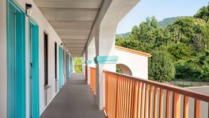 A corridor with teal doors and a wooden railing overlooking a forested hillside.