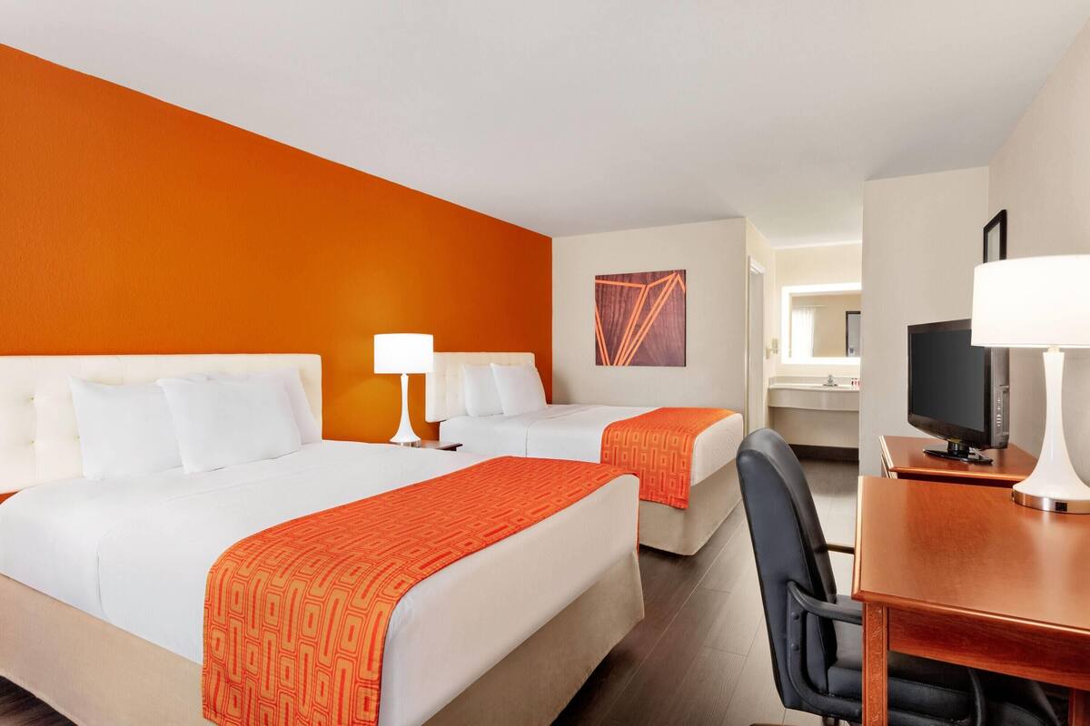 Een hotelkamer met twee bedden, een bureau met een televisie, en een badkamer op de achtergrond.
