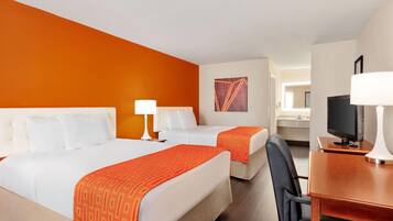 A hotel room with two beds, a desk with a television, and a bathroom in the background.