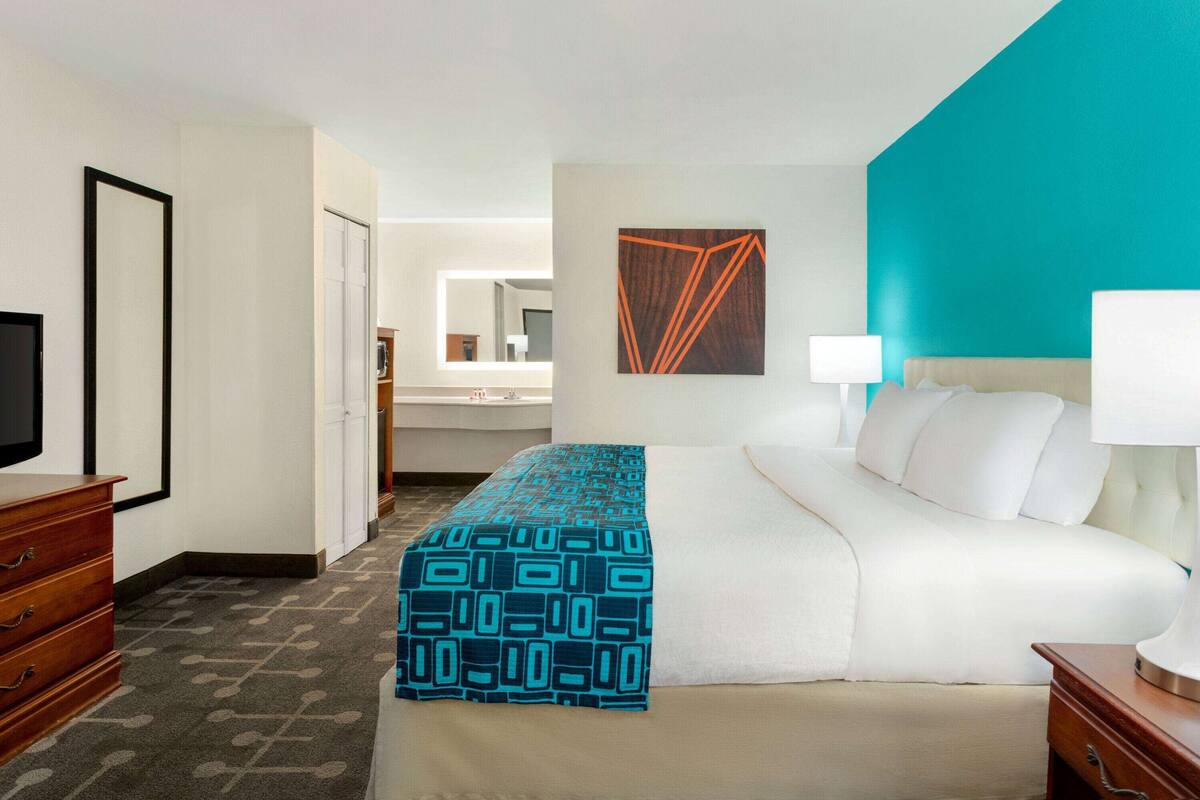 Hotelkamer met een bed, een televisie, een dressoir, een badkamer op de achtergrond en een wand in teal kleur.
