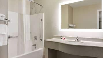Un baño con ducha a nivel, bañera, lavabo y un espejo grande.