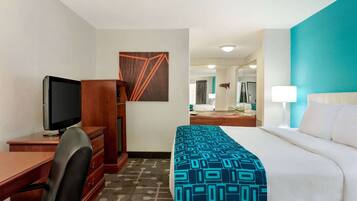 Une chambre d’hôtel avec un lit, un bureau avec une télévision, une chaise, une commode et une salle de bain visible au fond.