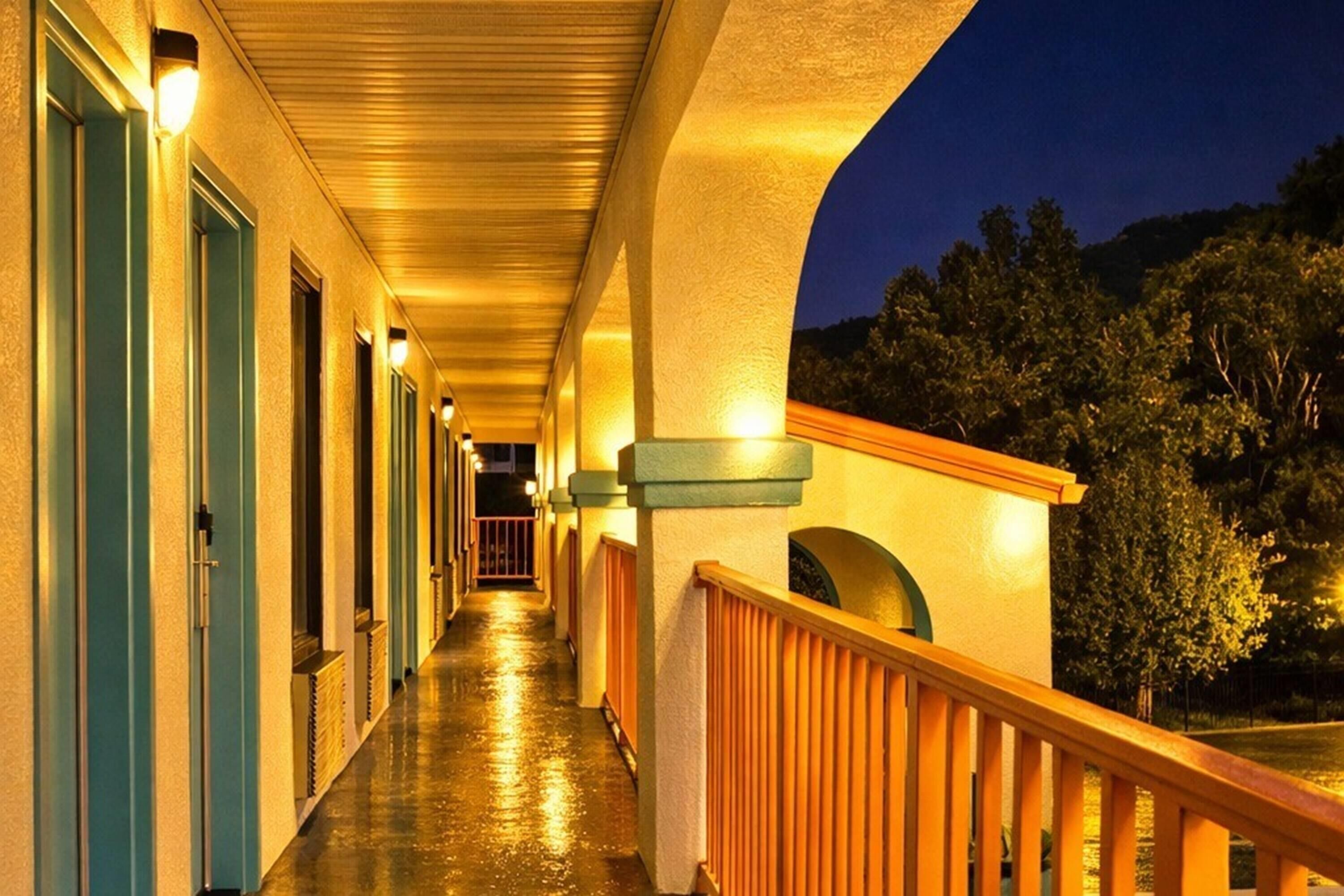 Un pasillo de hotel con puertas, una barandilla de madera y un cielo nocturno.