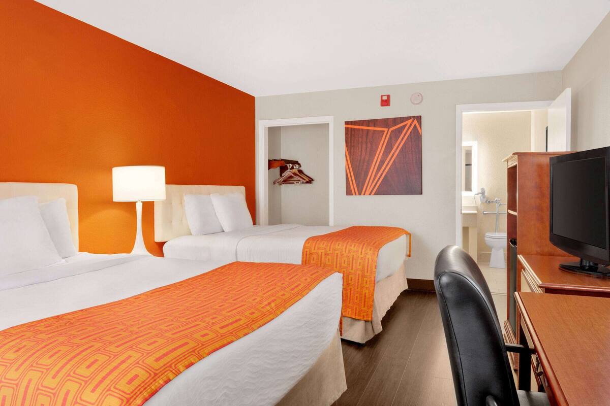 Hotelkamer met twee bedden, een televisie, een bureau en een badkamer zichtbaar door een geopende deur.