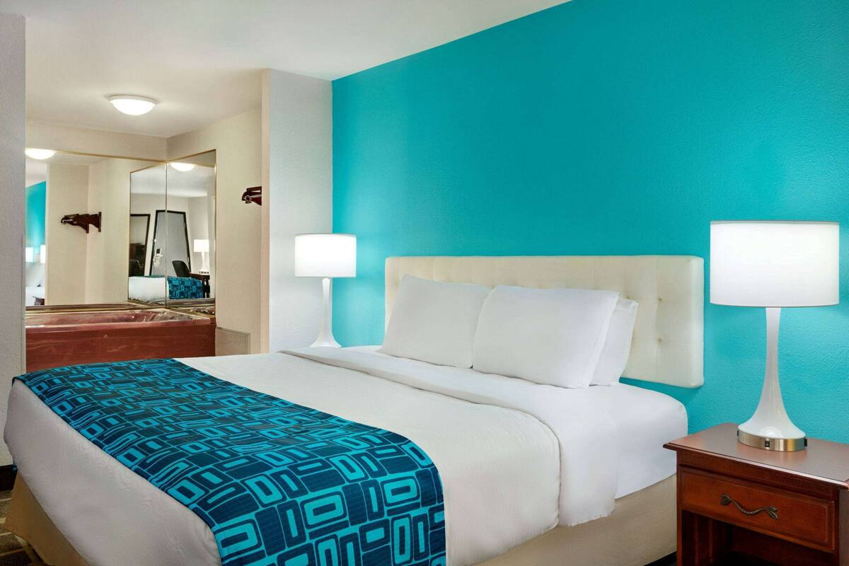 Een hotelkamer met een bed, twee bedlampen, een nachtkastje en een spiegel.